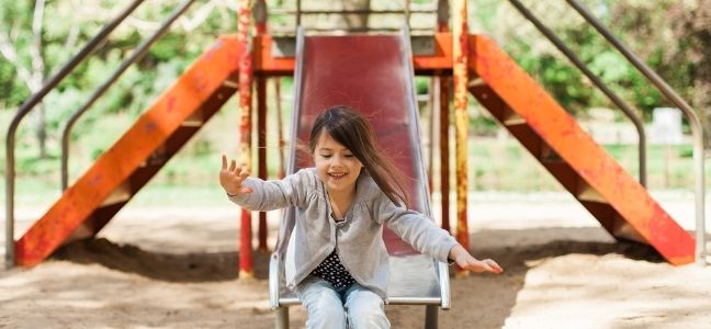 Three slides in a kids playground with a young person sliding down the middle one